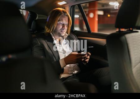 Businessman using mobile phone in car at night Stock Photo