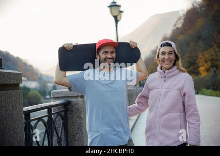 Man holding skateboard standing with woman near railing on footpath Stock Photo