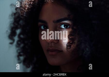 Serious young woman with curly hair in dark Stock Photo
