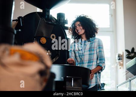Smiling owner standing near machine in coffee roastery Stock Photo
