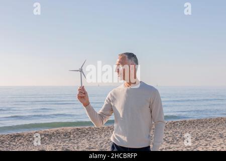 Man looking at wind turbine model standing on beach Stock Photo