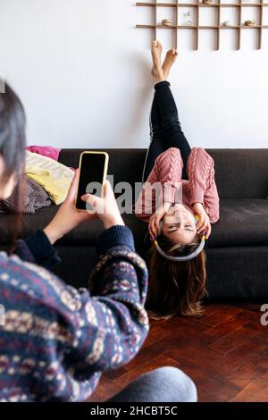 Young woman photographing friend through mobile phone at home Stock Photo
