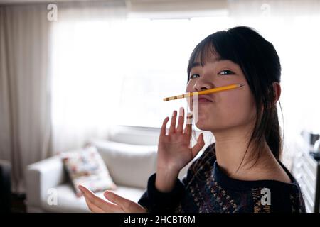 Young woman holding pencil on puckered lips at home Stock Photo