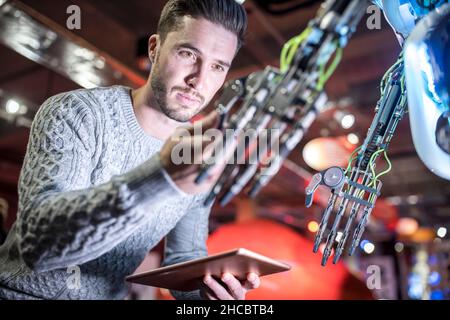 Engineer examining robotic arm holding tablet PC at workshop Stock Photo