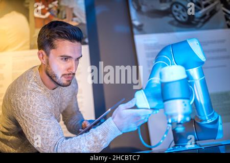 Technician programming robotic arm holding tablet PC at workshop Stock Photo