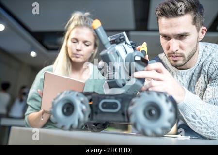 Engineer repairing combat car with colleague programming at workshop Stock Photo