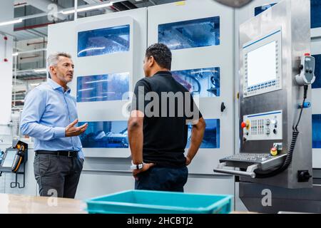Businessman explaining engineer by machine in industry Stock Photo