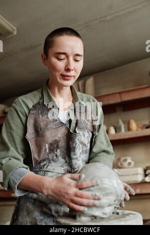 Young woman creating clay sculpture on special equipment working in ceramic studio Stock Photo