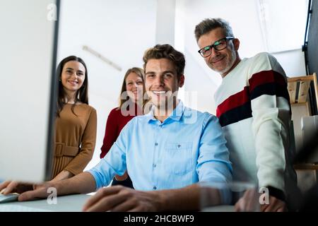 Young businessman using desktop PC with colleagues standing at desk in office Stock Photo