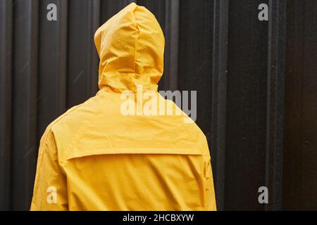 Medium back view shot of unrecognizable man wearing yellow raincoat standing outdoors on rainy day Stock Photo