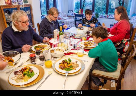 A family sit together at a dinning table and eat a roast Christmas dinner. Stock Photo