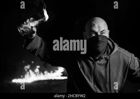 A masked man is holding a burning bottle. Molotov cocktail. Stock Photo