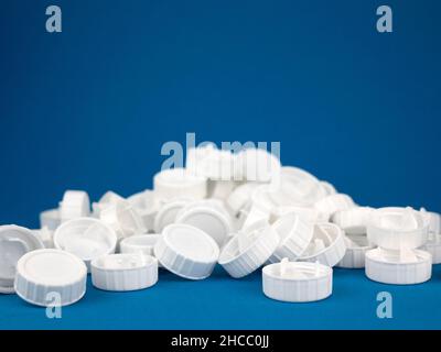 Pile of white plastic screw caps on the blue background, selective focus. Closures made from renewable polymers. Concept of waste sorting and plastic Stock Photo
