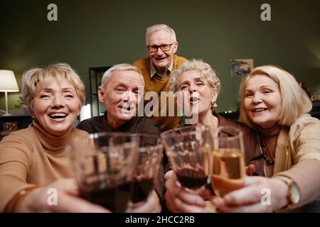 POV of five aged friends looking at camera while holding and clinking wine and champagne glasses during festive dinner Stock Photo