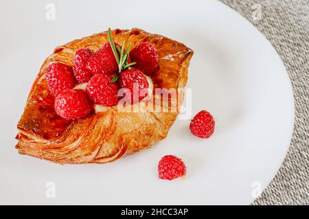 Close up of Raspberry and custard pastry tart on a white dish with two berries on the side Stock Photo