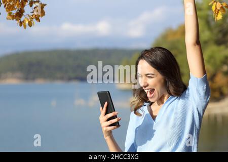 Excited woman checking smart phone celebrating good news outdoors Stock Photo