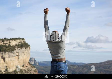 Back view portrait of an excited man with black skin raising arms in nature Stock Photo