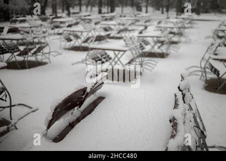 Tables and chairs suites of closed Bavarian beer garden in public park in Regensburg in winter with fresh snow Stock Photo