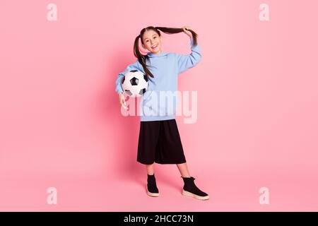 Full length body size photo of schoolgirl in sport outfit keeping ball smiling cheerful isolated pastel pink color background Stock Photo