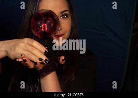 Woman observing physics through a plasma lamp that glows in the dark with magenta highlights Stock Photo