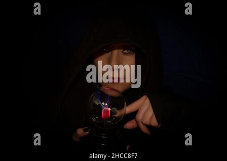 Alternative woman with nose piercing looking at camera surrounded by fantasy and mystery dressed in hoodie pointing to neon of plasma lamp with magent Stock Photo