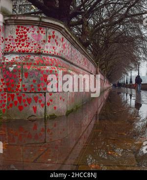 London, UK 26th December 2021. The National Covid Memorial Wall reflected in puddles on a rainy day. Over 150,000 red hearts were painted by volunteers and members of the public, one for each life lost to coronavirus in the UK.