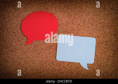 Two speech bubbles, one round, one square laying on a cork board. Close up. Stock Photo