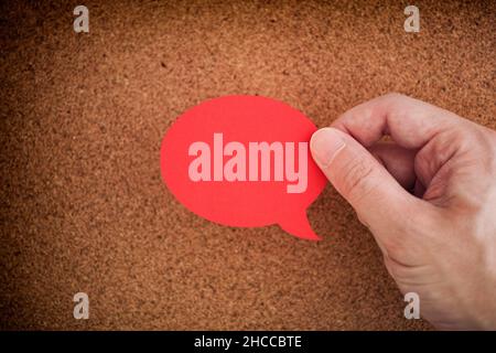 A man holding a red speech bubble in his hand above a cork board. Close up. Stock Photo