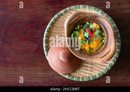 Baked poached eggs with cheese spinach scallions in clay pot on a bamboo plate Stock Photo