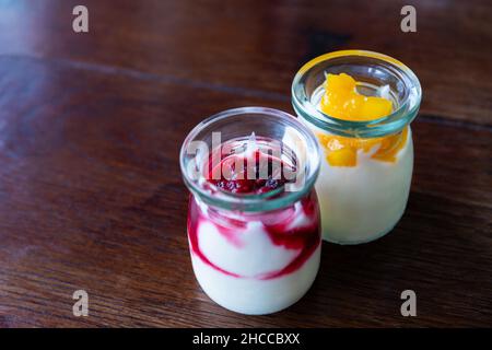 Greek yogurt with berries and mango in glass jars on wooden background Stock Photo