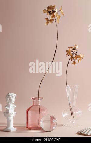 simplicity, naturalness, wabi sabi concept. dry flowers in vases on beige background. fashionable colored glass objects.  Stock Photo