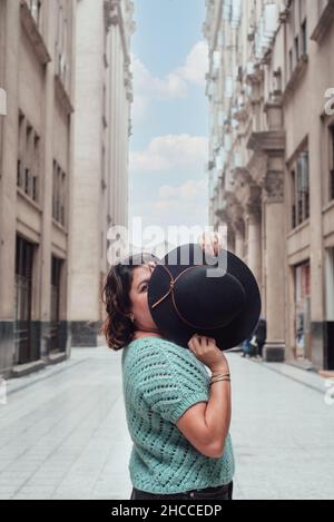 Woman who looks with only one eye and the other half of her face hides it with a black hat. Funny picture. Copy space Stock Photo