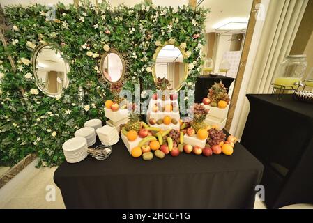 Banquet table of boxes of fruits and table settings in front of a decorated wall with mirrors Stock Photo