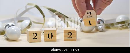 Hand is turning wooden cubes from 2021 to 2022 for the new year in panoramic format, seasonal decoration against a gray background, copy space, select
