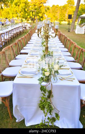 Long rustic style table with a white tablecloth and floral decorations in the beautiful garden Stock Photo
