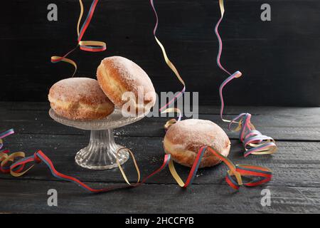 Berliner doughnuts or Krapfen with colorful party streamers on a dark rustic wooden table, traditional pastry for New Year or carnival, copy space, se Stock Photo