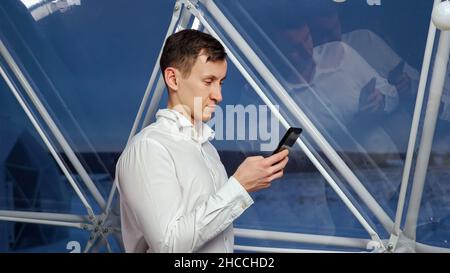 Man checks social media via phone against big glassy window Stock Photo