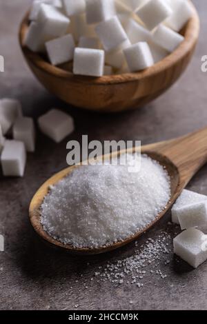 White crystal sugar in a wooden spoon and cube sugar next to it. Stock Photo