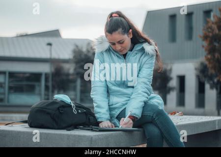 High school student girl making notes and writing sitting in the university center during her recess Stock Photo