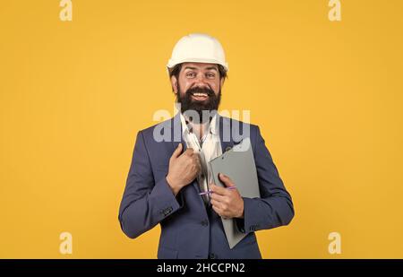 Man in a suit and construction helmet looking to the side and holding folder on yellow background, architecture Stock Photo