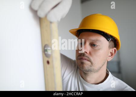 Man in helmet measuring wall using building level in apartment Stock Photo