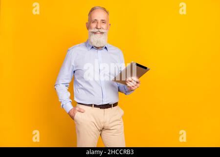 Photo of attractive cute age gentleman wear blue shirt standing holding modern device empty space isolated yellow color background Stock Photo