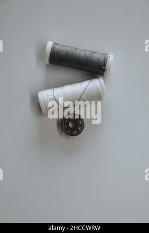 Two spools of white and gray thread and a button lie on a light background. Stock Photo