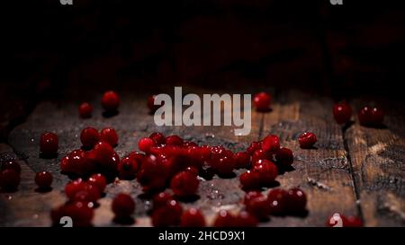 Close up of juicy red berries falling down on a dark brown old wooden table on black background, food preparation and gastronomy concept. Cranberries Stock Photo