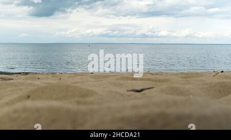 Close up of sandy shore and rippled sea on blue cloudy sky background. Natural background bird seagull flying slowly above the sea close to water surf Stock Photo