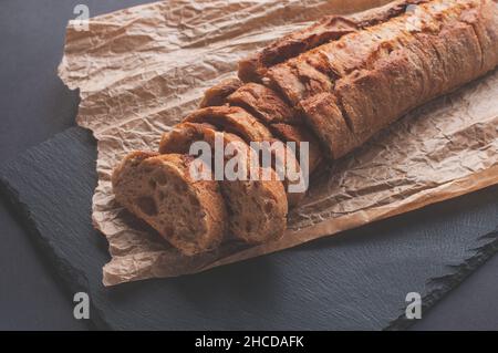cereal baguette cut into pieces on parchment paper on black background Stock Photo