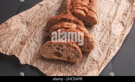 cereal baguette cut into pieces on parchment paper on black background Stock Photo