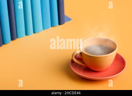 Yellow cup of coffee or tea with hot steam, on a yellow table, with light blue and blue books. Stock Photo