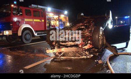 Haren, Germany. 28th Dec, 2021. Firefighters work on a car lying on its roof on the A31 motorway. A horse running loose on the motorway caused several accidents and a closure of the A31 in Lower Saxony on Tuesday night. According to the highway police, the animal had escaped from its trailer at the Haren junction and was initially hit by a 40-ton tractor-trailer. It was dragged along and ended up in the overtaking lane, where it collided with a car. The car skidded and landed on its roof. The horse did not survive. Credit: Ludger Tebben/Nord-West-Media/dpa/Alamy Live News Stock Photo