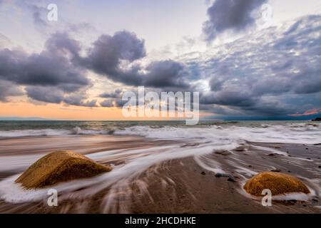 A Beautiful Ocean Sunset With a Colorful Sky As A Wave Rolls To The Sandy Shore Stock Photo